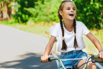 Obraz premium Child riding bicycle. Little kid girl on bicycle along bikeway. Happy cute little girl riding bicycle. Child cycling on bicycle.