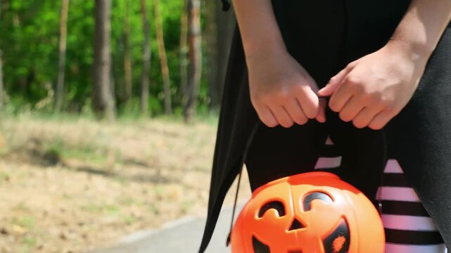 Halloween girl in witch costume. Trick-or-treating. Guising. Child in carnival outdoors. Celebrate halloween. Child Girl in forest smiling and holding basket of sweets