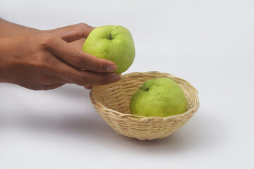 Someones hand is picking up green guavas in a fruit basket on a white background