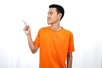 Portrait of a young Asian man wearing an orange t-shirt pointing aside copy space for promotional space. isolated on white background.