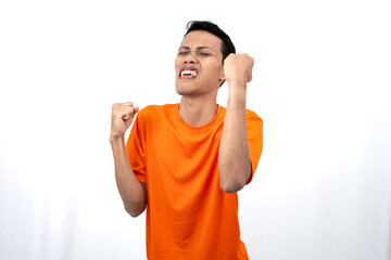 Portrait of a young Asian man wearing an orange t-shirt with a happy expression, surprised to get...