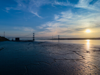 Suspension bridge standing over dried cracked muddy riverbed at sunset
