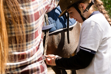 Young rider focused on adjusting horse saddle.