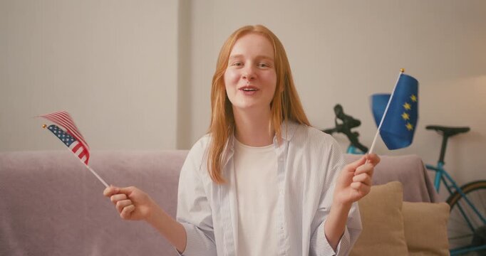 Red-haired woman waves EU and US flags lounging on sofa