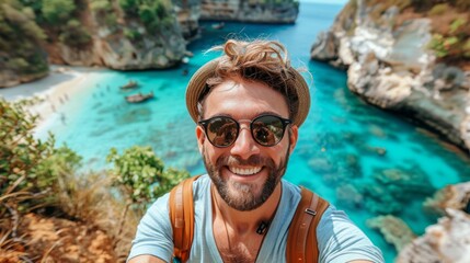 A young male travel video blogger vlogger wearing sunglasses takes selfies against the backdrop of a beach on a tropical island