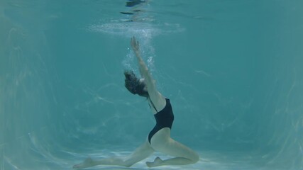 Elegant flexible athletic attractive woman training artistic swimming skills, stretching in pigeon position underwater while exercising in swimming pool.