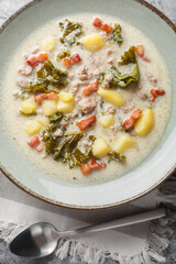 Meaty creamy zuppa toscana soup with Italian sausage, bacon and vegetables closeup on the plate on the table. Vertical top view from above