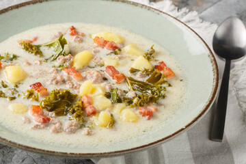 Italian traditional soup Zuppa Toscana with sausages, kale, potatoes and bacon close-up in a plate on the table. Horizontal
