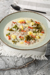 Zuppa Toscana hearty Tuscan Soup loaded with Italian sausage, kale, fried bacon and potatoes closeup on the plate on the table. Vertical