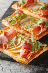 Puff pastry sandwich with pear, ham and arugula close-up on marble board on table. Vertical
