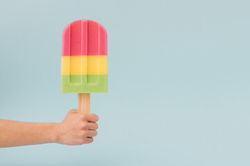 A hand holds a large ice cream on a light blue background. Minimal summer concept.
