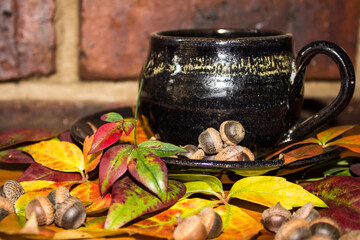 Teacup surrounded by autumn colored Virginia creeper leaves and tine acorns.