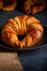 appetizing croissant placed on a black plate on top of a burlap cloth.