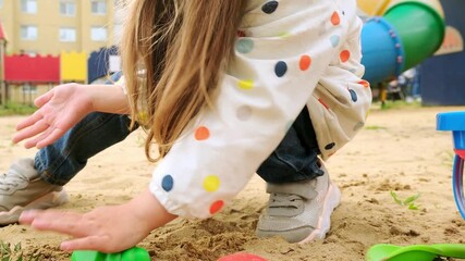 Little girl in the sandbox and plays with a shovel and sand. A child plays outside on a summer day. A child girl is sitting in the sandbox.