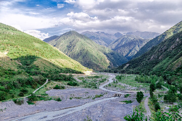 Fototapeta premium Almaty National Park, Kazakhstan. A mountain river meanders through a gorge against the backdrop of mountains and huge clouds