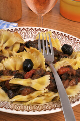 Farfalles aux courgettes et olives noires servies dans une assiette avec un verre de vin