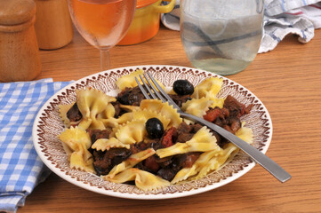 Farfalles aux courgettes et olives noires servies dans une assiette avec un verre de vin