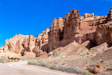 Fototapeta premium Great Charyn Canyon, Almaty, Kazakhstan. Valley of Castles. Bright blue sky with white clouds over a desert canyon on a hot, sunny day with sparse vegetation. Without people