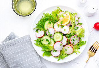 Summer vegan crispy salad with cucumbers, radishes and lettuce, white background, top view