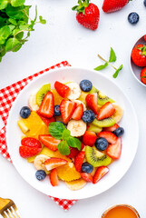 Summer vegan fruity salad with strawberries, blueberries, banana, kiwi, orange and mint on white background, top view