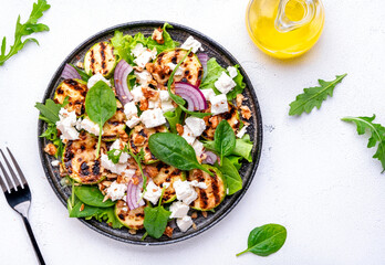 Summer grill salad with zucchini, feta cheese, nuts, onion, arugula and spinach on white background, top view