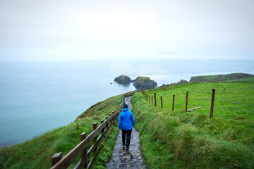 Frau mit blauer Jacke und blauer Mütze auf einem Wanderweg an den Klippen an der Küste am Meer...