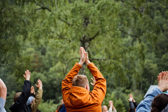 A group of people are standing in a circle with their hands in the air enjoying the natural landscape. They seem to be having a leisurely and recreational time in the forest during an event