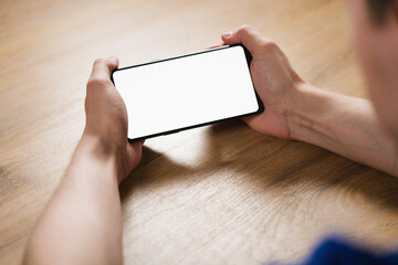 young man hands holding smartphone with blank white screen in landscape mode