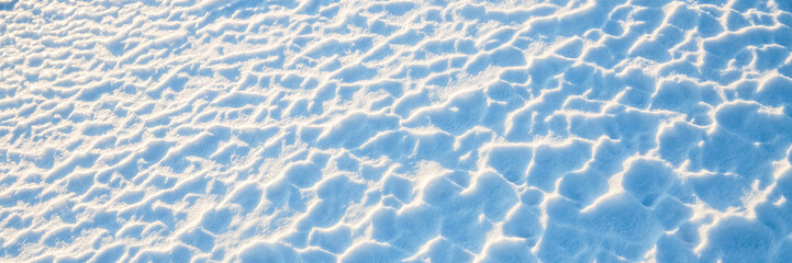 Beautiful winter background with snowy ground. Natural snow texture. Wind sculpted patterns on snow surface. Wide panoramic texture for background and design.