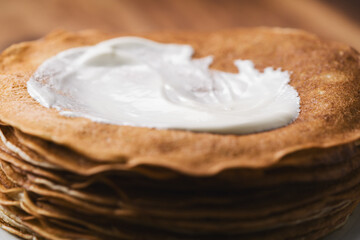 close-up of stack of fresh hot crepes or blinis with sour cream on wood table
