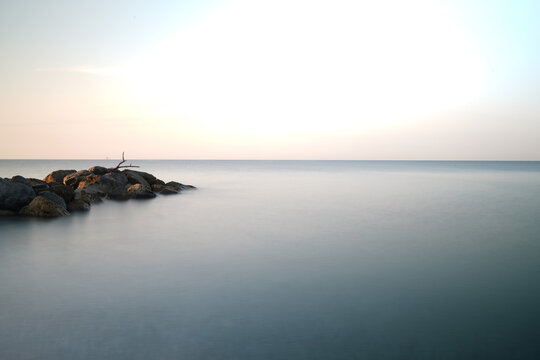 Alba poetica al mare con uno scoglio a sinistra in lunga esposizione che tutto appaia come in un sogno che porta alla pace interiore ed all'amore universale