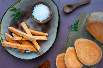 Raw sweet potato or yam, cut into slices, arranged on a plate and cutting board with spices.