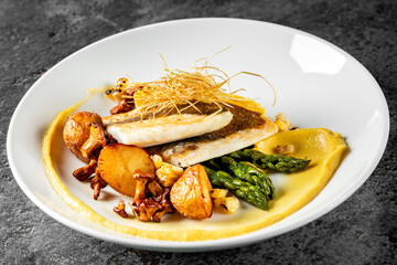Gourmet dish featuring seared fish fillet, asparagus, potatoes, and chanterelle mushrooms on a white plate with sauce. Elegant presentation suggests fine dining experience. Ideal for culinary