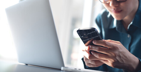 Asian business woman using mobile phone,  surfing the internet during working on laptop computer at modern office. 