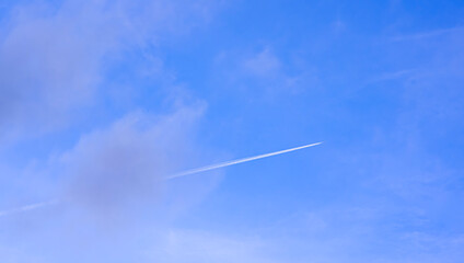 Jet airplane is flying with white contrail passing through the cloud on blue sky background