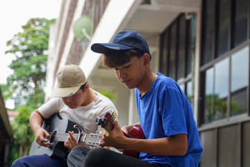 Fototapeta premium Young Asian male playing ukulele with friends during break from school. They are happy and relaxed. Concept of teenagers, friends, leisure activities.