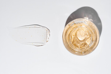 View from above, a jar of light textured moisturizer 24k gold gel in a glass jar on white background. Gel smear stroke next to it. Scene for advertising various skincare creams or sleep masks