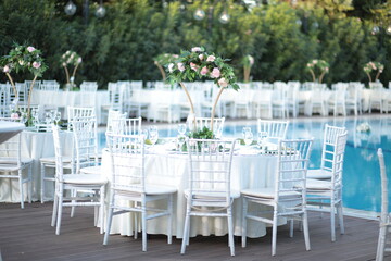 A romantic poolside wedding reception with lush floral arrangements and white chairs