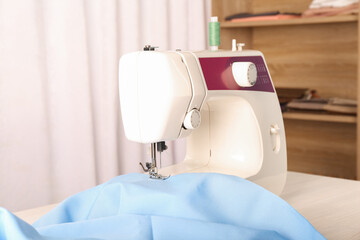 White sewing machine with light blue fabric on table indoors