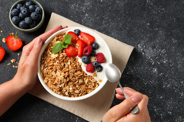 Woman eating tasty granola with berries and yogurt at dark textured table, top view