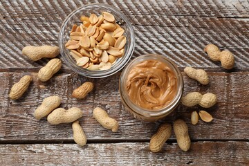 Tasty peanut butter in jar and groundnuts on wooden table, flat lay