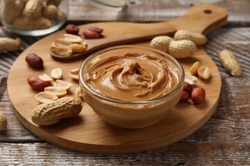 Tasty peanut butter in bowl and groundnuts on wooden table
