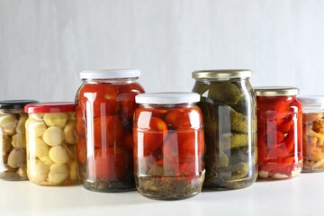Tasty pickled vegetables and mushrooms in jars on white background
