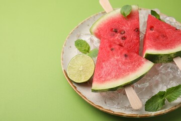 Pieces of tasty watermelon, ice cubes, lime and mint on green table, closeup. Space for text