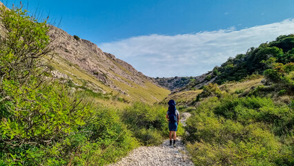 Man with baby carrier backpack entering gorge Vrzenica (Žig Vrženica)  in Baska, Krk Otok, Primorje-Gorski Kotar, Croatia. Scenic hiking trail through dramatic canyon leading to Vela and Mala Luka