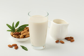 Fresh almond milk in glass, nuts, green leaves and pitcher on white background