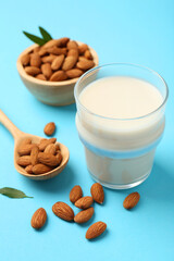 Fresh almond milk in glass, nuts, spoon and green leaves on light blue background