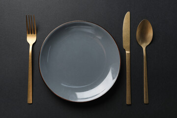 Elegant golden cutlery and plate on black background, flat lay
