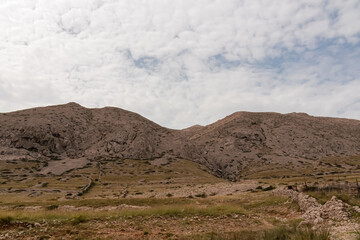Panoramic view of rolling hills and rugged mountains peaks covered in  patchwork of golden grasslands and sparse vegetation in Vela Luka bay on island Otok Krk, Primorje-Gorski Kotar, Croatia. Hiking