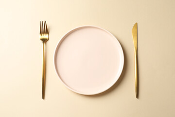 Stylish golden cutlery and plate on beige background, top view